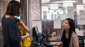 woman opening backpack and speaking to circulation desk staffer